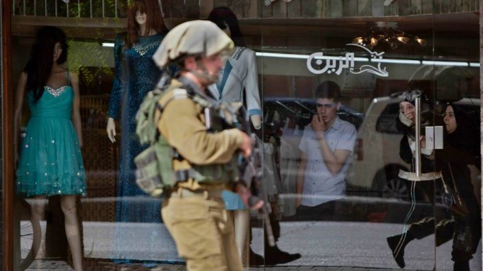 Un soldato israeliano dell'Idf cammina in una via di Hebron alla ricerca delle telecamere di sicurezza installate nei negozi palestinesi per capire se è possibile riuscire a recuperare i filmati e trovare tracce dei tre giovanissimi rapiti (foto di Majdi Mohammed/Ap)