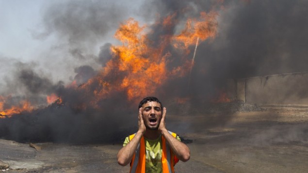Un vigile del fuoco di Gaza City vicino alle fiamme in un deposito delle Nazioni Unite dopo l'attacco israeliano (foto Mahmud Hams/Afp)