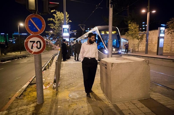 Un ebreo ultraortodosso camminate di fianco a uno dei blocchi di cemento messi alle fermate del tram di Gerusalemme per evitare altri assalti dei palestinesi a bordo delle auto (foto Flash 90)